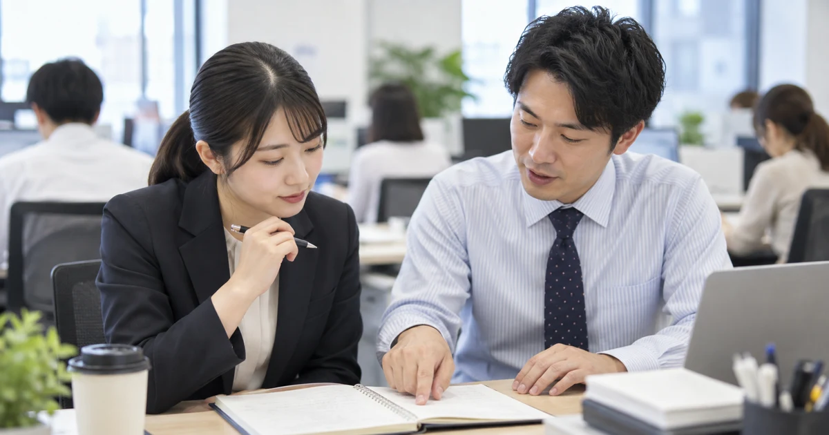 転職初日に先輩社員とデスクで業務メモを確認する人