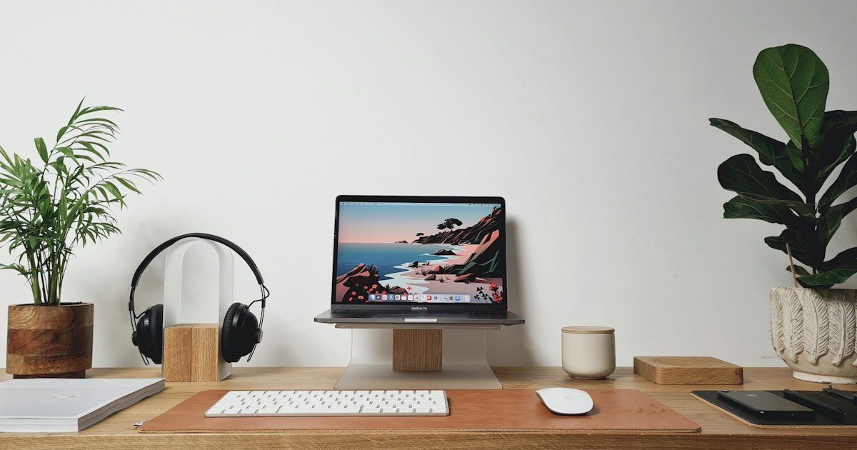 植物のある机に並べたノートパソコンとヘッドホン、白いキーボード